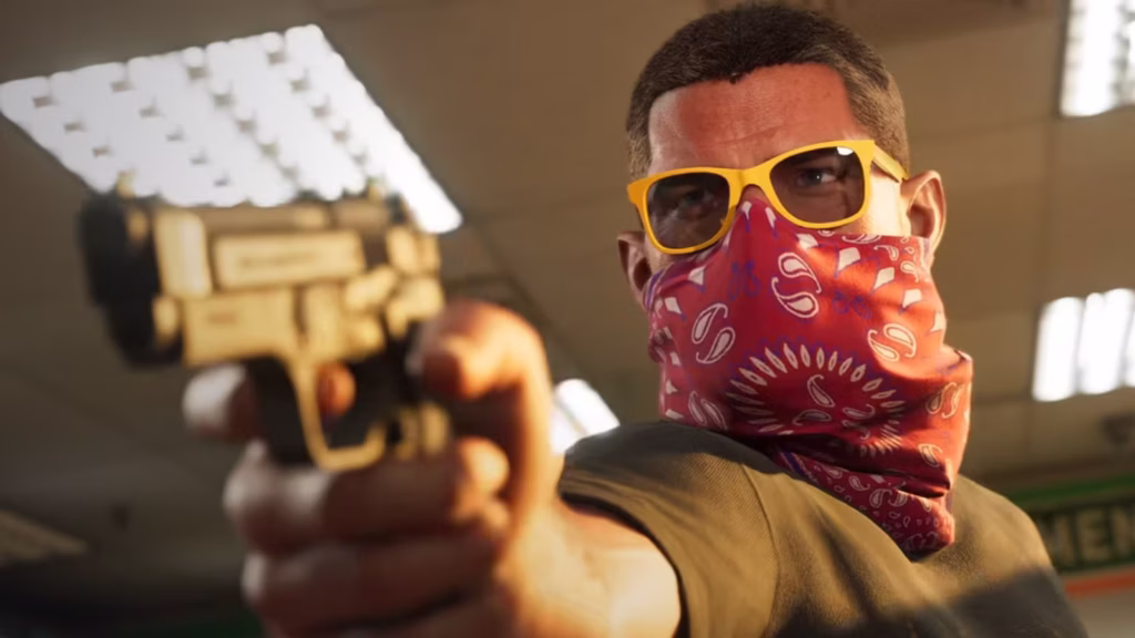 A close-up image of GTA 6 protagonist Jason pointing a gun at the camera inside a well-lit convenience store. He has a red bandana covering his mouth and nose, yellow sunglasses on his head, and a focused, intense expression. The image is taken from Trailer 1.