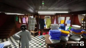Balts 3D tēls ar melnu smaidošu seju stāv telpā, kurā redzami drēbju pakaramie un salocīti krāsaini dvieļi.