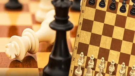 Master Chess game banner featuring a split design. The left side displays a dramatic close-up of a fallen white king chess piece resting on a polished wooden board next to a standing black queen. The right side shows a top-down, isometric view of a digital chessboard with a tan and brown square pattern, showcasing white chess pieces aligned at the bottom rows and black pieces lined up at the top.
