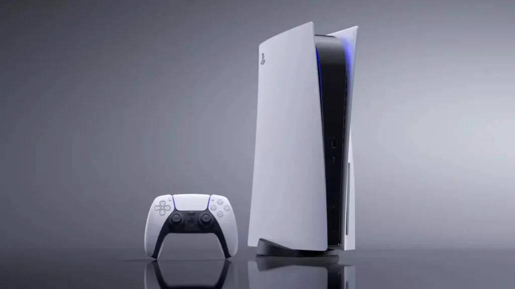 ertikāli novietota balta PlayStation 5 konsole ar spīdīgi melnu vidusdaļu un zilu apgaismojumu, tai blakus novietots balts DualSense kontrolieris uz pelēka fona ar vieglu atspulgu.