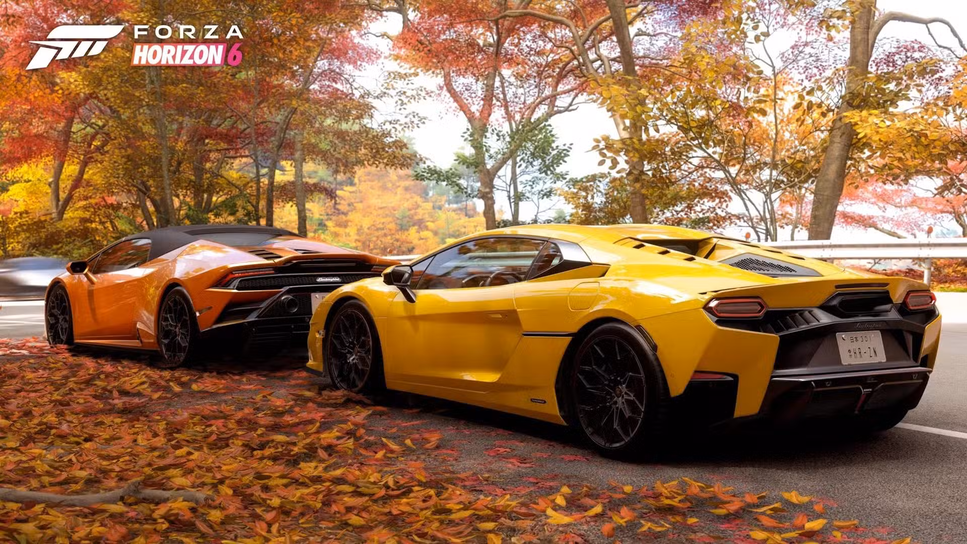 Divas sporta automašīnas – oranžs un dzeltens Lamborghini – brauc pa gleznainu Japānas ceļu, ko ieskauj koši rudenīgas koku lapas