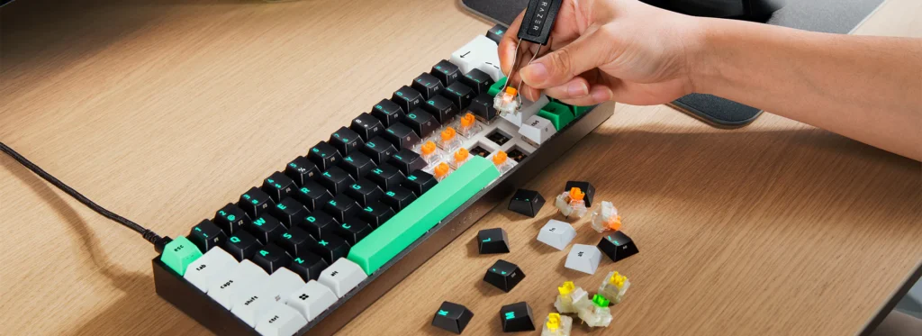 Lietotāja roka ar speciālu rīku izņem oranžu mehānisko slēdzi no Razer Reclusa X Mini 65% klaviatūras, kurai ir melni, balti un zaļi taustiņi.