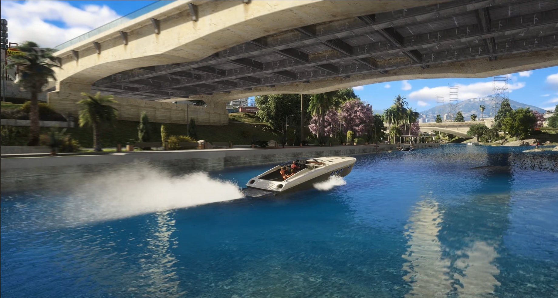 Motorlaiva brauc pa Los Santos River V2 kanālu zem betona tilta saulainā dienā ar Vinewood zīmi fonā